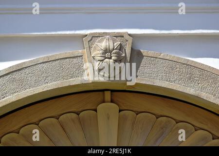 decorative stone arched beam above wood gates. Ornamental carved keystone with flower motive. textured white stucco exterior wall elevation closeup Stock Photo