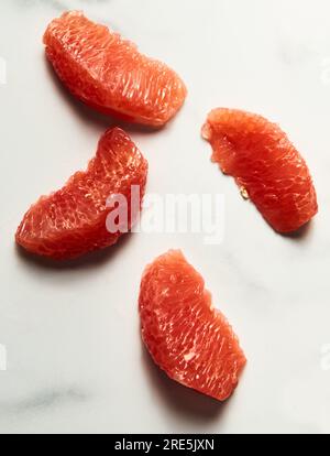 Peeled and sliced, divided in sections grapefruit on the white marble countertop. Bright, hey-key vertical photo.Top view food photo Stock Photo
