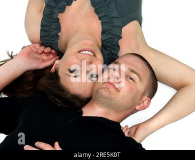 Handsome young couple lay besides each other on the floor.  Their heads are opposite of each other and they are affectionate, smiling and happy. Stock Photo