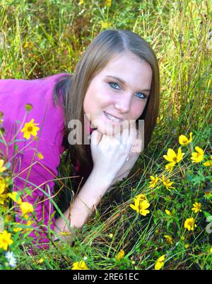 Laying in a meadow of wildflowers, young woman smiles and enjoys her early morning communing with nature. Stock Photo