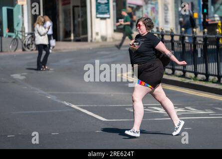 Overweight young lady crossing a busy road in England, UK, looking happy, jolly, colourful and confident. Stock Photo