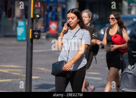 Young woman walking in busy urban area speaking on a mobile phone or cell phone, in Summer in England, UK. Stock Photo