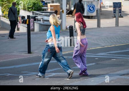 Pair of young slim women, girls or teenagers, dressed in jeans, walking across a road and going shopping in Summer, UK. Friends at shops. Stock Photo