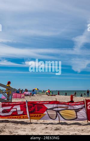Big wind screen on the beach by the sea. Spectacles picture on the wind shield. Baltic Sea, Rowy, Poland. Hot summer day. Crowds. Stock Photo