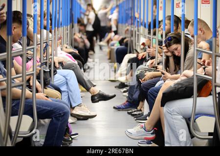 Crowd of people in a metro train in summer, passengers sits with smartphones. Interior of subway car Stock Photo