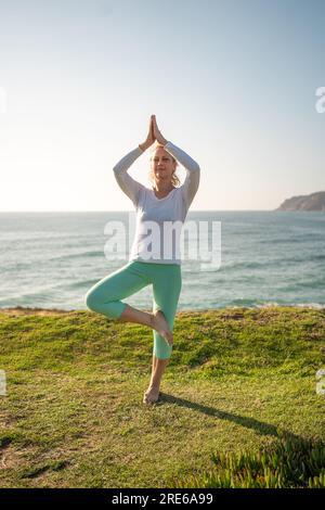 Yoga woman standing in vrikshasana tree pose hand namaste on cliff at ...