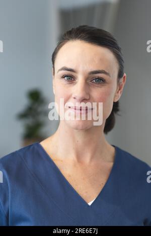 Portrait of happy caucasian female doctor wearing blue scrubs in corridor at hospital Stock Photo
