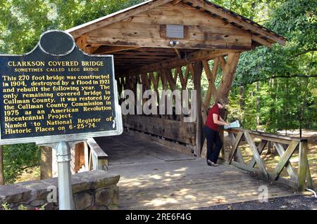 Female visitor to the Clarkson Covered Bridge looks at map of the area.  She has on a red plaid shirt.  Information sign stands in front of bridge. Stock Photo