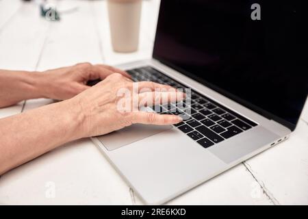 Close up of mature woman's hands working with laptop at the table of outside cafe. Middle-aged lady works and plays using modern technology. Active li Stock Photo