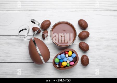 Delicious chocolate eggs, paste and candies on white wooden table, flat lay Stock Photo
