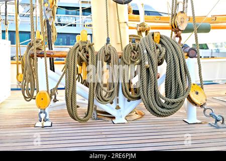 Hempen lines neatly coiled on a beautiful vintage classic sailing ship. Beautiful teak planks of the deck and big wooden blocks and shackles at the ba Stock Photo