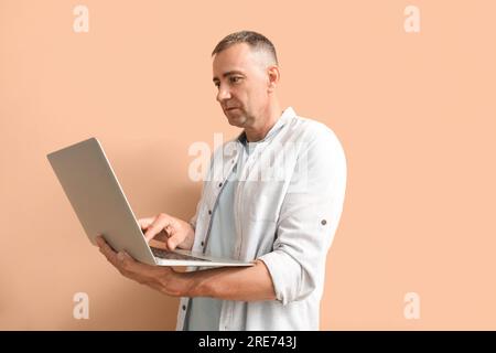 Mature male programmer with laptop on beige background Stock Photo