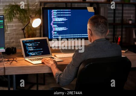 Mature male programmer working in office at night, back view Stock Photo