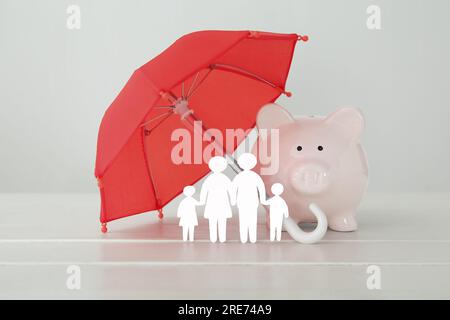 Figures of family with umbrella and piggy bank on white wooden table. Insurance concept Stock Photo