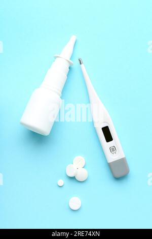 Pills, nasal spray and thermometer on blue background Stock Photo
