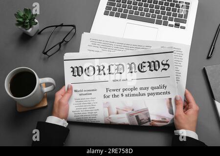 Woman reading newspaper at workplace with coffee and laptop on grey background Stock Photo