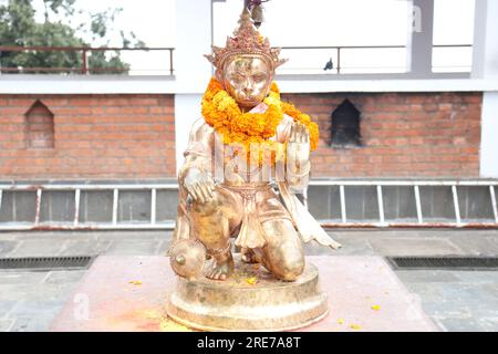 Hanuman statue in sitting position with natural brick wall background made up of bronze material and decorated with colour full flowers Stock Photo