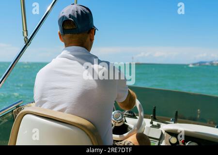 Bach view of middle-aged man driving luxury motor yacht. Captain at the helm of motor boat. Image with selective focus Stock Photo