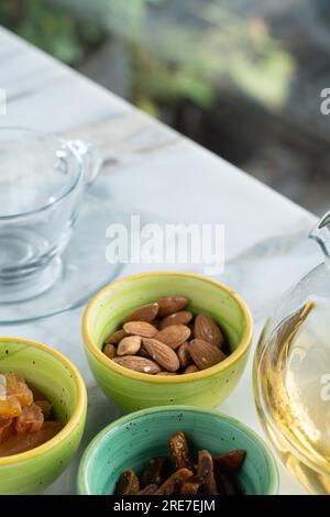 Dried fruits in a small round glass bowl next to a glass on a ceramic table. Delicious and healthy drink. Selective focus. Stock Photo