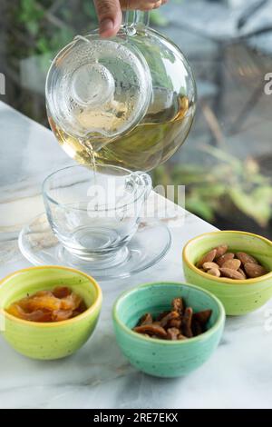Dried fruits in a small round glass bowl next to a glass on a ceramic table. Delicious and healthy drink. Selective focus. Stock Photo