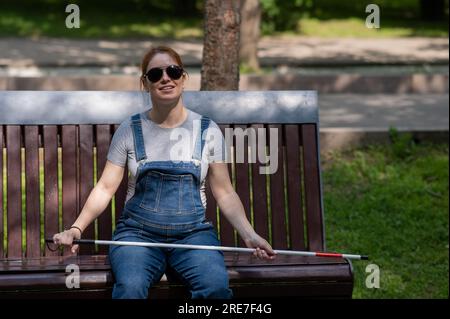 Blind red-haired pregnant woman sitting on a bench outdoors.  Stock Photo