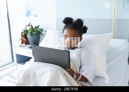 African american girl patient lying on bed using tablet in patient room at hospital Stock Photo