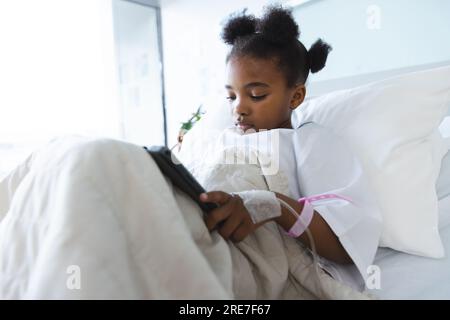 African american girl patient lying on bed using tablet in patient room at hospital Stock Photo