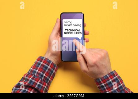 Man received message Sorry We Are Having Technical Difficulties on smartphone on yellow background, top view Stock Photo