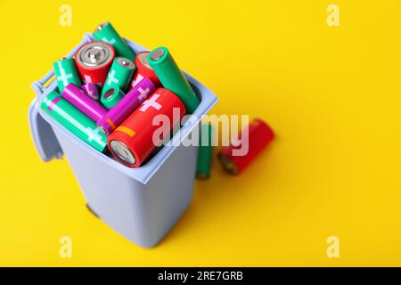 Many used batteries in recycling bin on yellow background, closeup. Space for text Stock Photo
