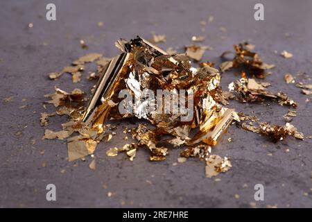 Many pieces of edible gold leaf on grey textured table, closeup Stock Photo