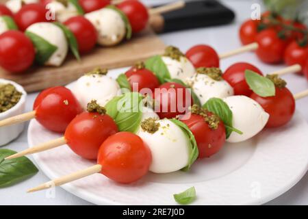 Caprese skewers with tomatoes, mozzarella balls, basil and pesto sauce on table, closeup Stock Photo