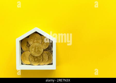 Model of a wooden white house with bitcoins on a yellow background. The concept of buying real estate, saving on a house, financing construction Stock Photo