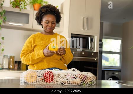 Happy plus size african american woman unpacking groceries in kitchen Stock Photo