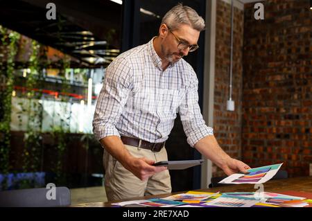 Caucasian businessman holding a digital tablet reading documents on a wooden table at modern office Stock Photo
