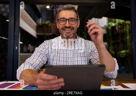 Portrait of a caucasian businessman smiling while using a digital tablet at modern office Stock Photo