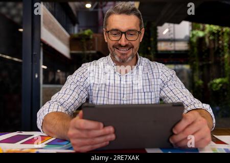 Caucasian businessman smiling while using a digital tablet at modern office Stock Photo