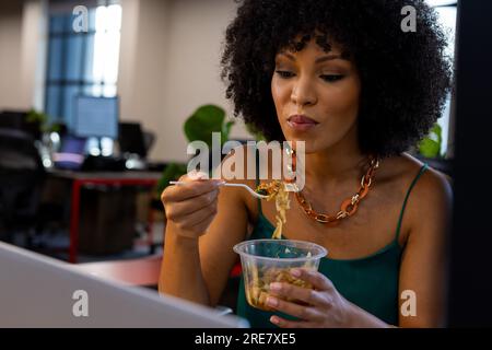 African american woman having a snack sitting on her desk at office Stock Photo