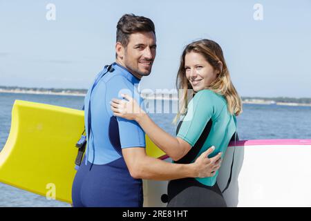 couple in wetsuits looking back towards camera Stock Photo