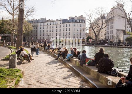 People sit out along the canal in the up-and-coming Canal Saint Martin area of Paris, on a beautiful spring day. Stock Photo