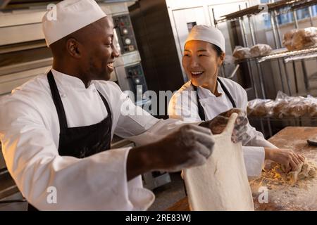 Happy diverse bakers wearing aprons in bakery kitchen and preparing dough Stock Photo