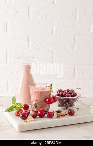 Freshly made homemade cherry smoothie in a bottle and a large glass on a stone board podium with berries and mint leaves. Detox Stock Photo