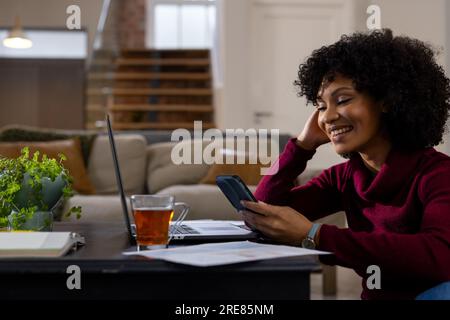 Happy biracial woman using laptop and smartphone at home Stock Photo