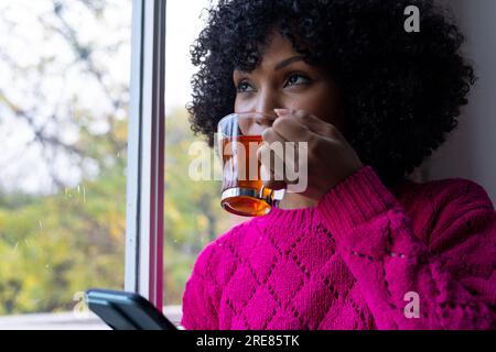 Biracial woman drinking tea and using smartphone at home Stock Photo