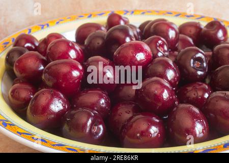 A close-up view of a bunch of juicy red cherries with water droplets on them, arranged on a ceramic plate with a floral pattern. A delicious and healt Stock Photo