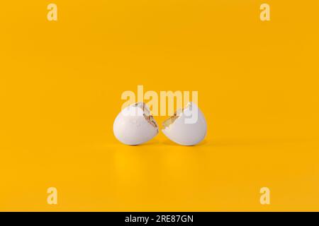 Broken white eggshell on a bright yellow background. Minimalist conceptual image of a cracked egg shell representing a new beginning or fragile life. Stock Photo