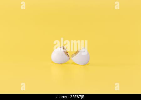 Broken egg shell on a bright yellow background. Minimalist cracked white eggshell on yellow. Empty cracked Easter egg on a yellow background. Stock Photo