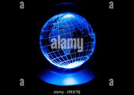 World map model engraved with a laser inside a glass globe. World map with blue neon light on isolated black background. Earth and finance concept. Stock Photo