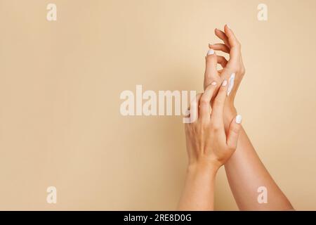 Beautiful young woman hands with cosmetic cream. Woman applies cream on her hands on beige background, copy space Stock Photo