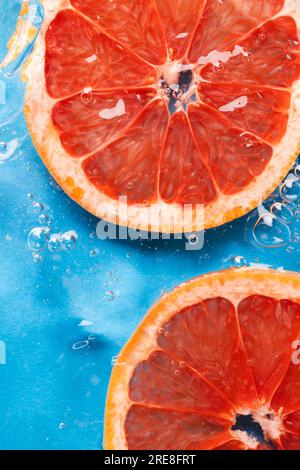 Close up of red grapefruit slices in water with copy space on blue background Stock Photo