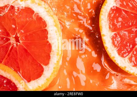 Close up of red grapefruit slices in water with copy space on orange background Stock Photo